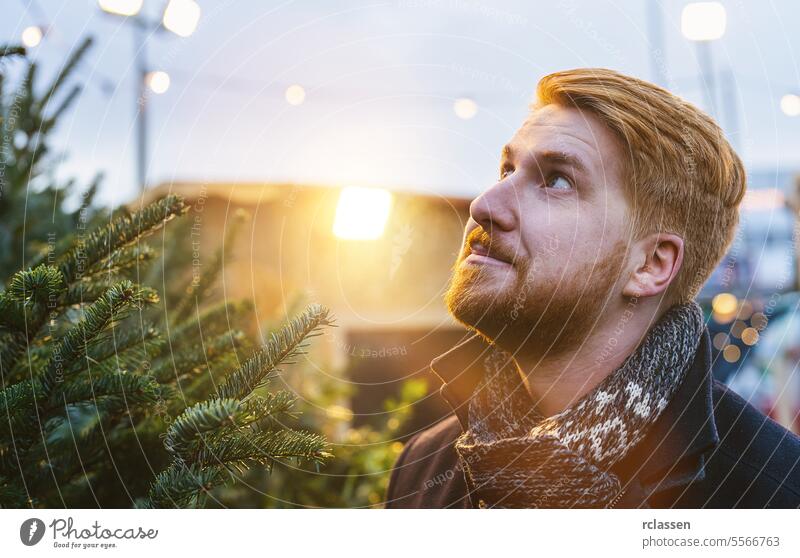 Redhead man looks skeptical which Christmas tree they should choose to buy at the Christmas tree sale, copy space for text facial expression looking up family