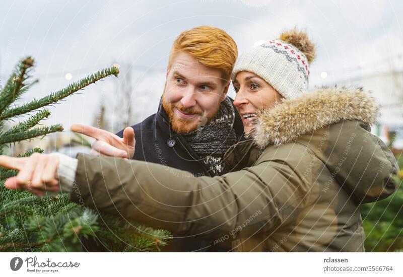 couple looking to buy a Christmas tree and points his finger to his selected tree pointing finger family skeptical redhead tradition choice smile man