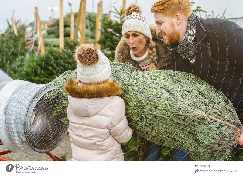 Happy Family being wrapped up a cut Christmas tree packed in a plastic net at a christmas market teamwork buy help child daughter safety net bagged bind