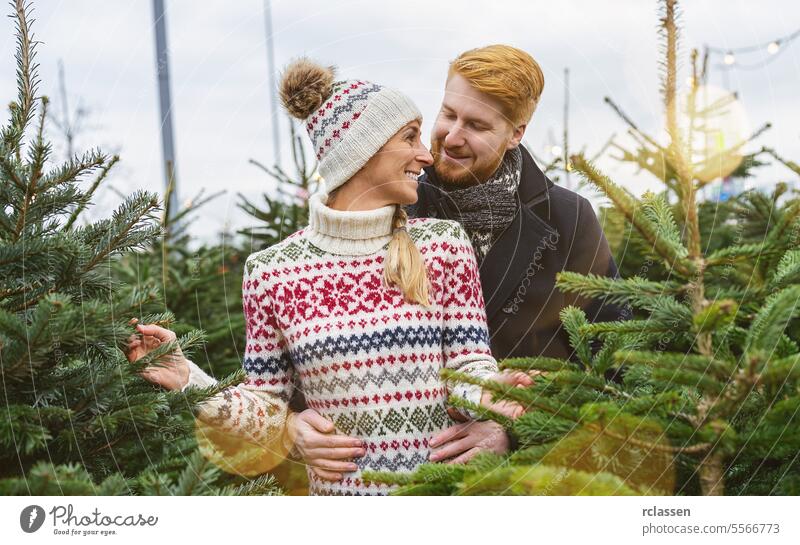 happy couple in love buying christmas tree at street market in evening. winter holidays and people concept image look at kiss family redhead tradition choice