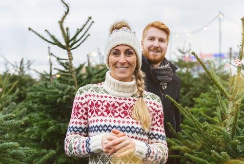Happy couple at a market want to buy a Christmas tree and look into the camera looking surprised family happy redhead tradition choice smile man love couple