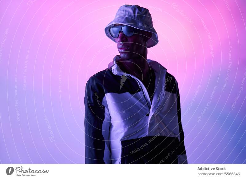 Stylish black man in hat and glasses posing in glowing studio young stylish outfit model studio shot sunglasses carefree standing cool attitude fashion light