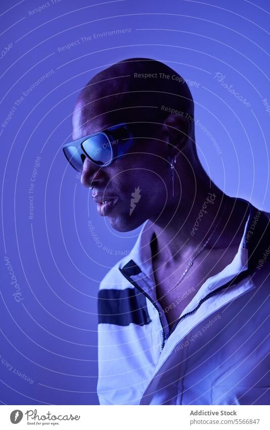 Bald male model with sunglasses posing on blue background man young stylish bald confident casual attire looking piercing emotionless outfit standing