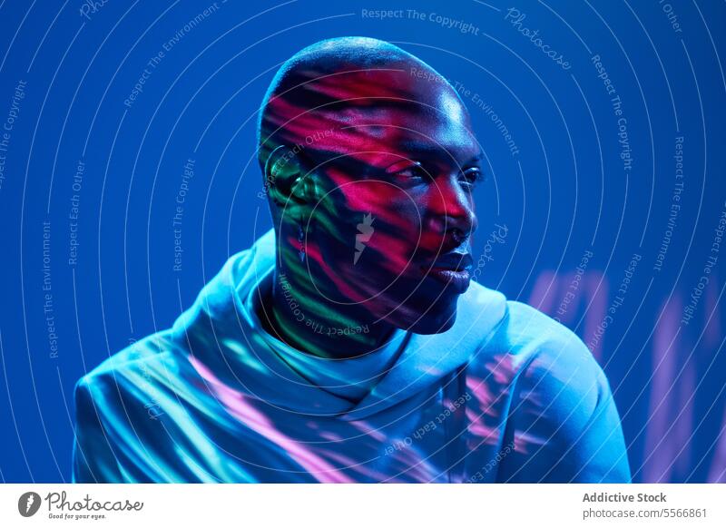 Black man thinking and looking away over blue background young bald thoughtful light glow face earring piercing trendy serious confident portrait model