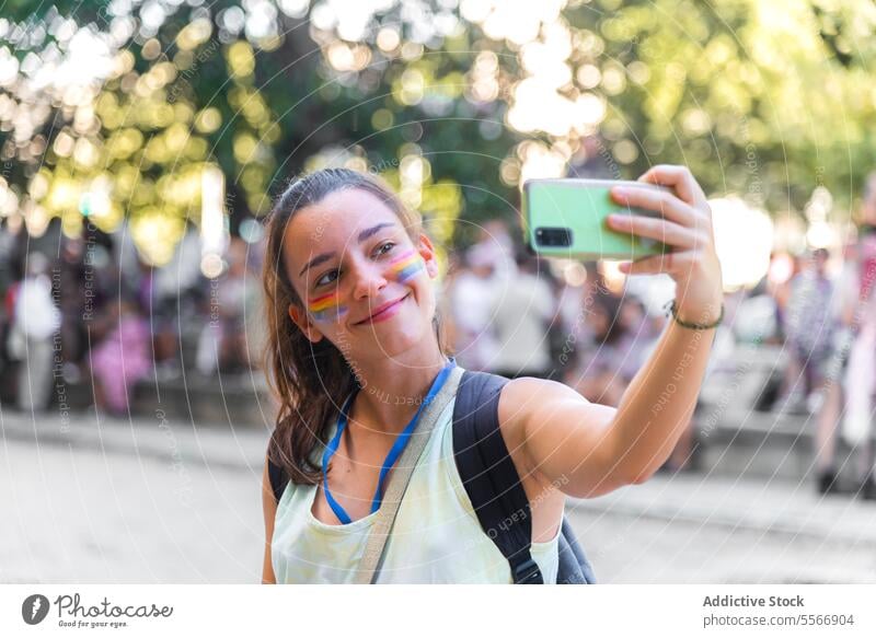 Woman taking selfie at pride event woman outdoors face paint stripe joy phone smile celebration day blurred background attendee festival young camera capture