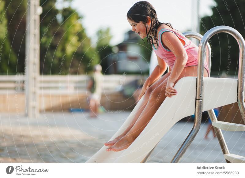 Girl enjoying a slide at the outdoor poolside. swimsuit striped fun summer sun play white day laugh water descend metal handrail excitement activity childhood