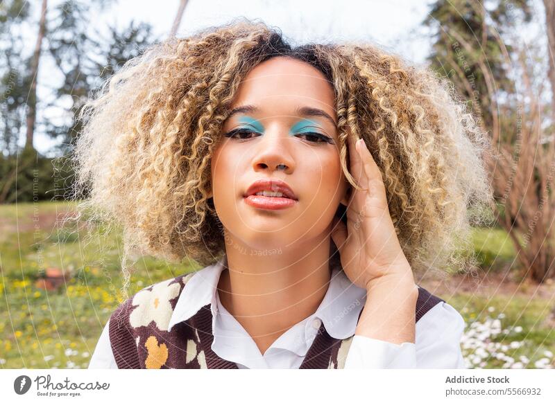 Young afro woman with turquoise eyeshadow and flower-patterned vest Woman blonde curly hair radiant hand white collar shirt sweater shape look beauty fashion
