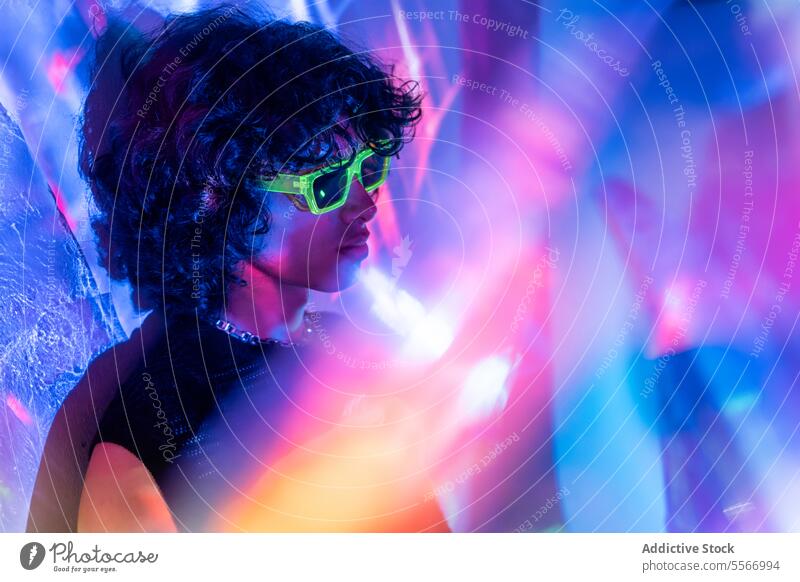 Contemplative latin man with neon shades among lights portrait sunglasses green curly hair contemplative vibrant hues young male fashion design urban modern