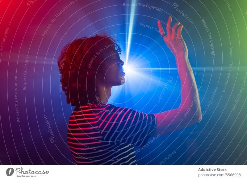 Latin man captivated by radiant blue light in moody setting virtual reality curly vr glasses hair striped futurist shirt reach latin red purple atmosphere glow