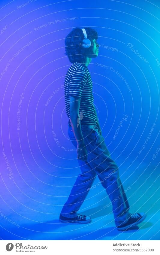 Curly-haired latin man with headphones immersed in blue ambiance curly striped shirt walk gradient music sound profile step stride fashion model atmosphere