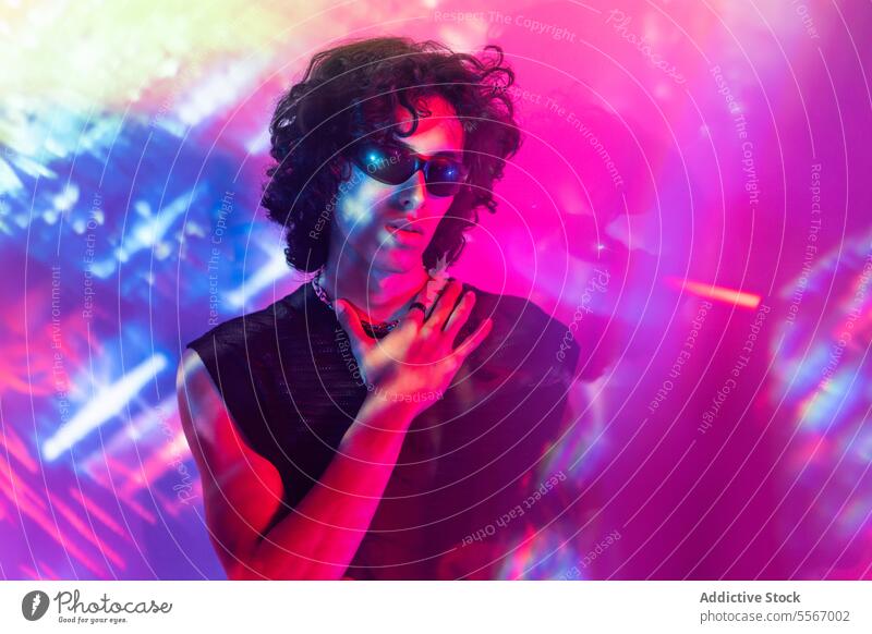 Latin man with sunglasses amidst vibrant neon spectacle colorful curly hair radiant latin pose lights reflection contemplative young male fashion atmosphere