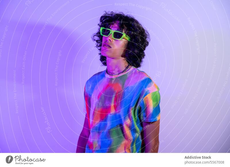 Latin man in vibrant tie-dye shirt and green shades latin curly hair sunglasses lilac backdrop fashion style casual color pose model urban male profile stand