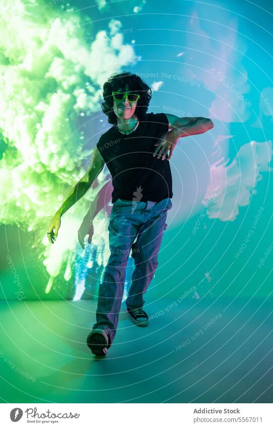 Dynamic leap of latin man amidst neon cloud ambiance green sunglasses motion energy jeans shirt casual style design modern light glow urban fashion trend studio