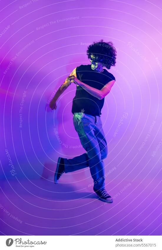 Energetic dance of latin man in neon-lit lilac background curly hair dynamic movement energy purple light accent vivid young pose rhythm expressive style motion