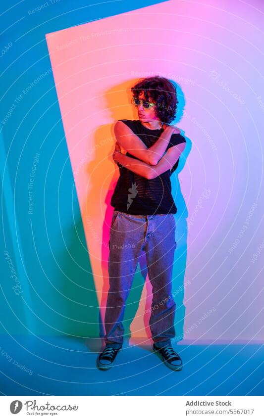 Confident stance against turquoise backdrop man latin individual curly hair sunglasses stand mesh top jeans confidence pose fashion style portrait casual mood