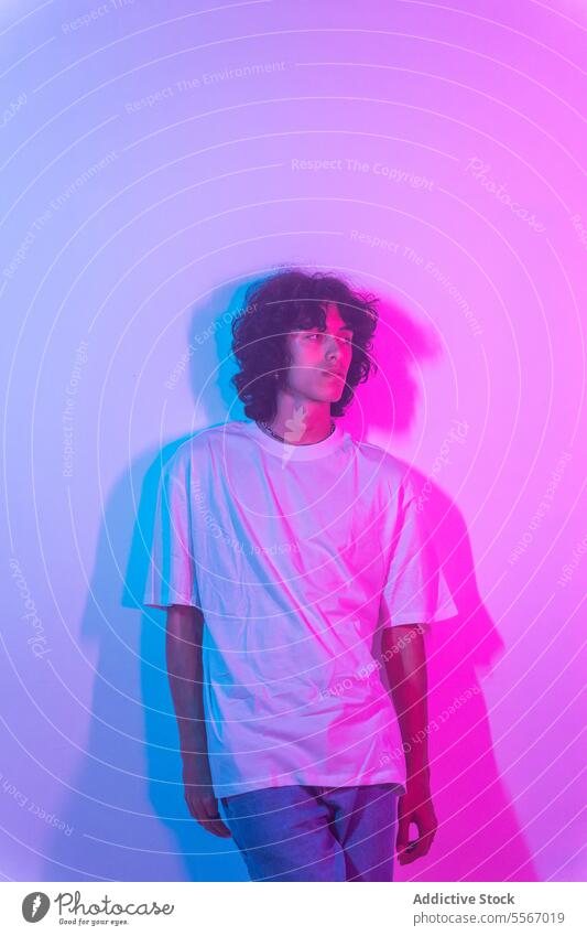 Curly-haired latin man in white against a gradient purple-blue backdrop curly shirt contemplative look stand fashion model studio light profile gaze youth style