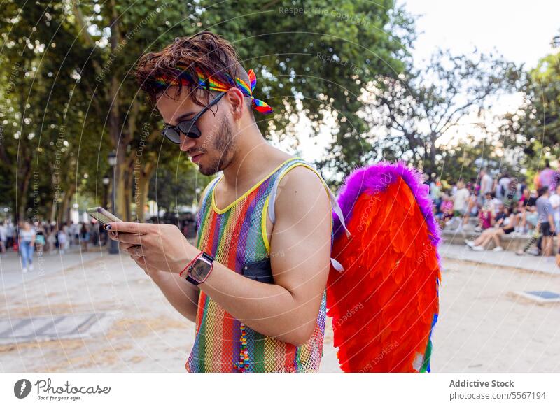Young man engaged in pride celebration lgbtq rainbow phone wing colorful gathering outdoor festival event text message crowd technology freedom expression