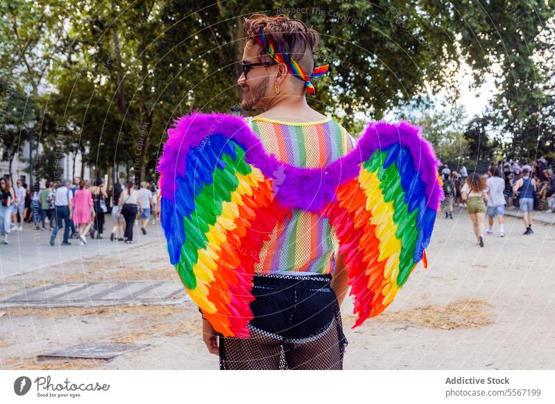 Prideful display in park man rainbow wing accessory LGBTQ pride crowd celebration vibrant color festival expression unity freedom symbol outdoors diversity