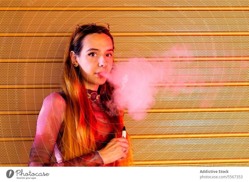 Young woman vapor exhales against orange backdrop background textured vibrant hair style attire confident young fashion smoke e-cigarette modern pattern