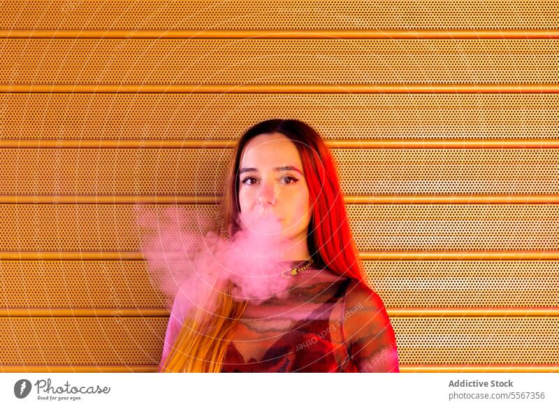 Young woman vapor exhales against orange backdrop background textured vibrant hair style attire confident young fashion smoke e-cigarette modern urban pattern