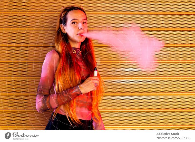 Young woman vapor exhales against orange backdrop background textured vibrant hair style attire confident young fashion smoke e-cigarette modern pattern