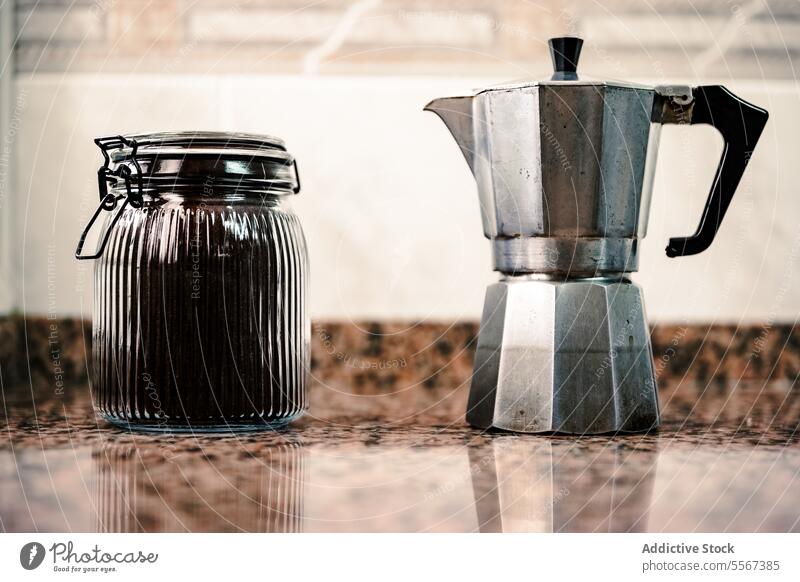 Glass jar and moka pot on granite glass coffee countertop kitchen clamp lid metal reflection Italian brew vintage silver ribbed texture handle beverage espresso