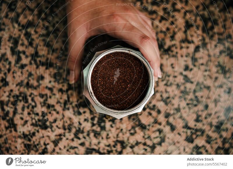 Fresh coffee grounds preparation hand espresso maker stovetop countertop close-up Italian jar seal stainless steel brew bean ingredient roasted aroma base grip