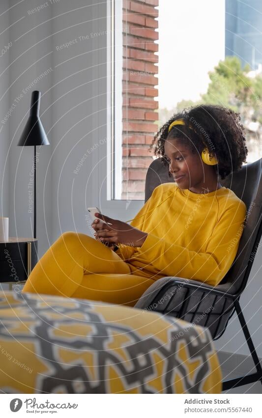 Black woman relaxed in city living yellow outfit apartment music headphones african american browsing modern interior female window chair ethnic urban using