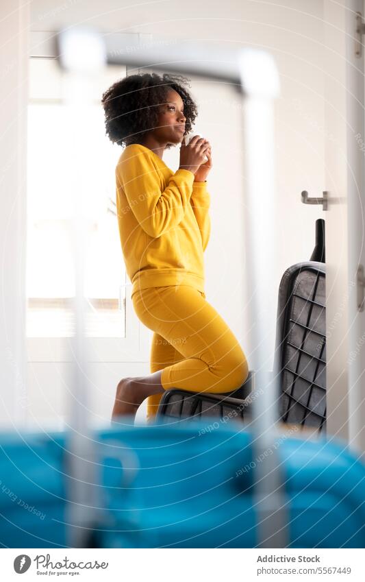 Black woman in contemplating travel yellow suitcase window contemplate journey young think lean curly hair indoor room reflection female black ethnic light home