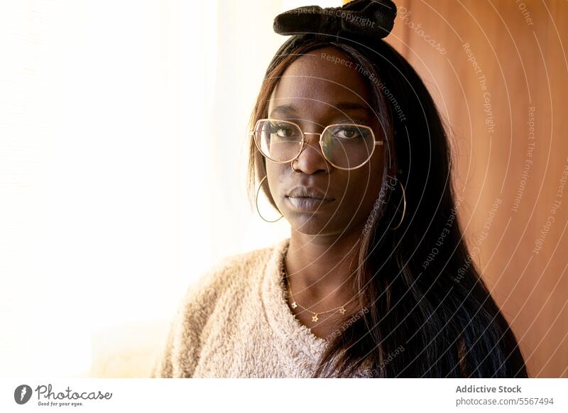 Thoughtful African American lady at home portrait eyeglasses headband black textured sweater light calmness thought focused serene stylish indoor woman
