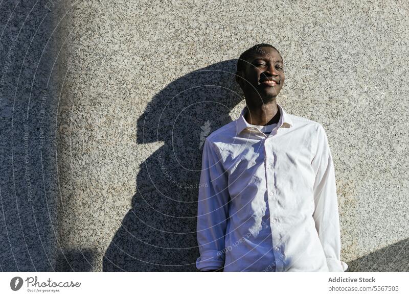 Smiling man in the sunlight smile shadow texture wall shirt face joy leaning urban outdoors white content serene pose happy male profile summer youth expression