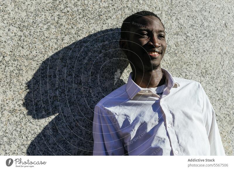 Smiling man in the sunlight smile shadow texture wall shirt face joy leaning urban outdoors white content serene pose happy male profile summer youth expression
