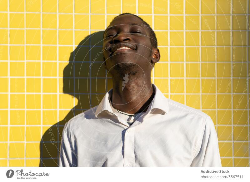 Young man with in Bright laughter young joyful yellow tile wall sunlight shadow white shirt bright vibrant happy cheerful positive emotion face teeth smile mood