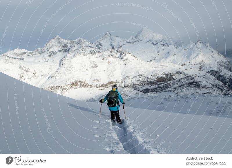 Anonymous person descending snowcapped mountain skier unrecognizable pole back view covering skiing effort challenge vacation active adventure swiss alps range