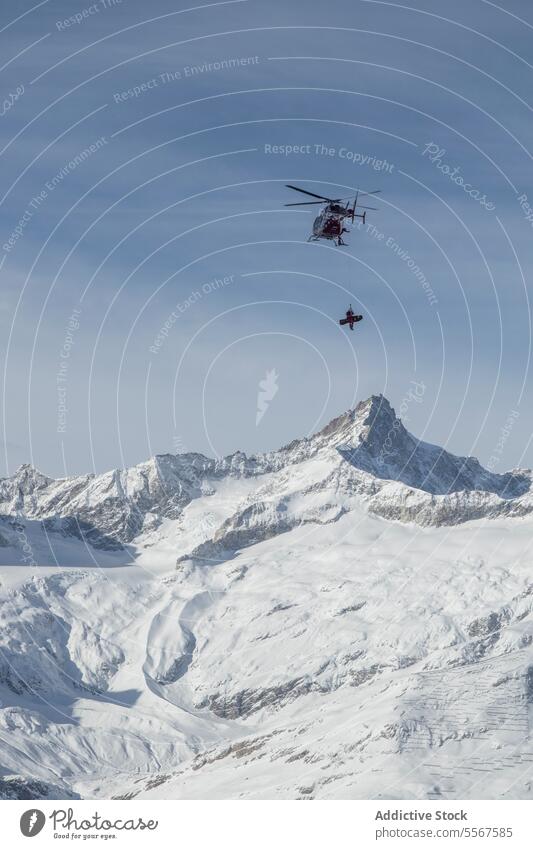 Snowboarder hanging from helicopter over snow mountain snowboarder flying travel covering transportation landscape sky swiss alps motion mid-air tourism