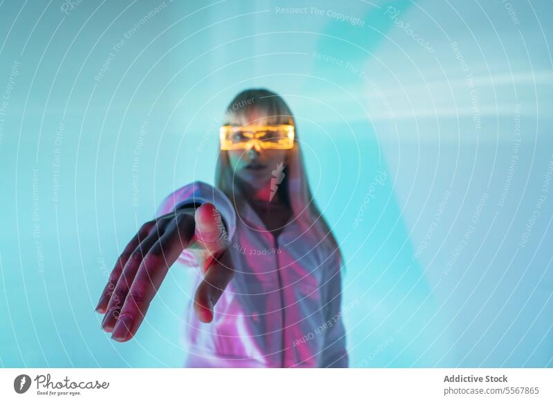 Woman in glowing VR glasses gesturing in studio woman modern vr goggles point hand experience immerse confident piercing virtual reality gesture led studio shot