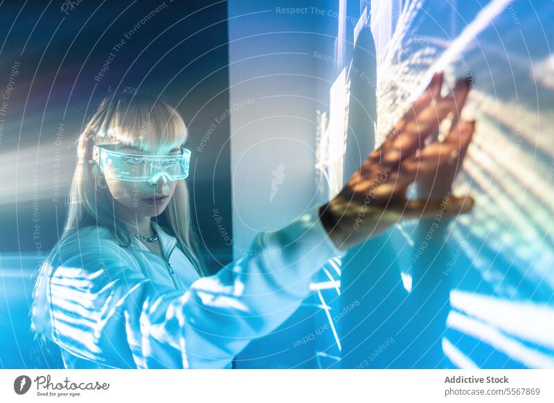 Woman in VR goggles touching wall with lights woman vr glasses futuristic explore cyberspace studio shot imagine long hair bangs trendy style blonde headset