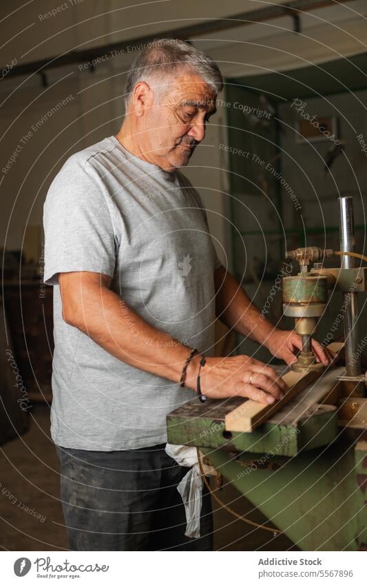 Carpenter at work in Toledo workshop man senior carpentry wood machinery tool male craft skill focus artisan workbench manual labor elderly equipment dedication