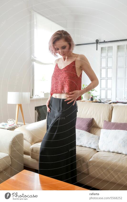 A Red-haired woman in fashion clothes standing at home redhead red-haired model skirt top living room posing fashion model person pretty dress elegant female