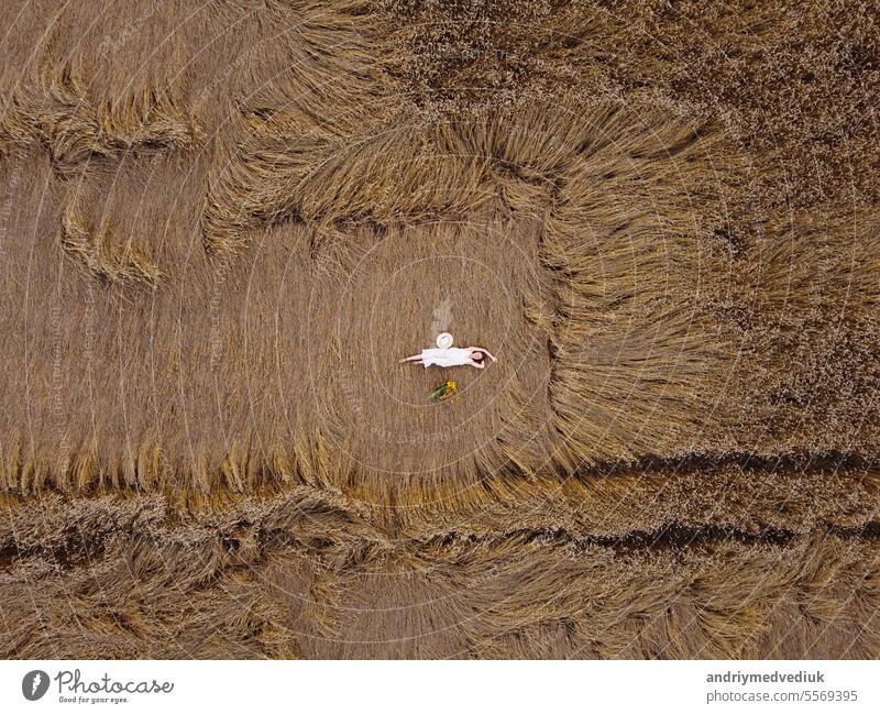 Aerial view of a pretty young woman enjoying the outdoors. girl wearing a white dress lying in wheat field. People, travel, freedom concept. female model nature