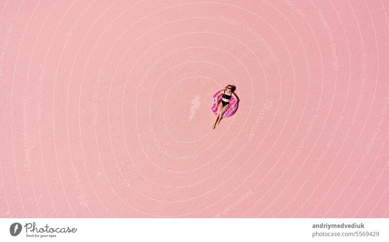 Aerial view of Beautiful woman lying in a bikini on inflatable mattress on pink salt lake. copy space. opening of the tourist season. summer holiday concept. taken from above from a drone
