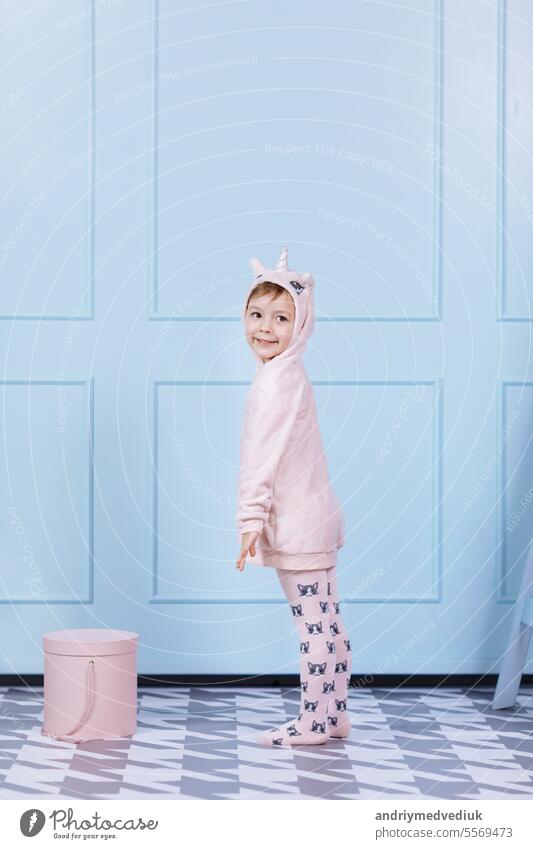 Smiling beautiful little girl in unicorn pink costume is smiling and having fun on a blue wall background. happy childhood. hat face cute kid adorable smile