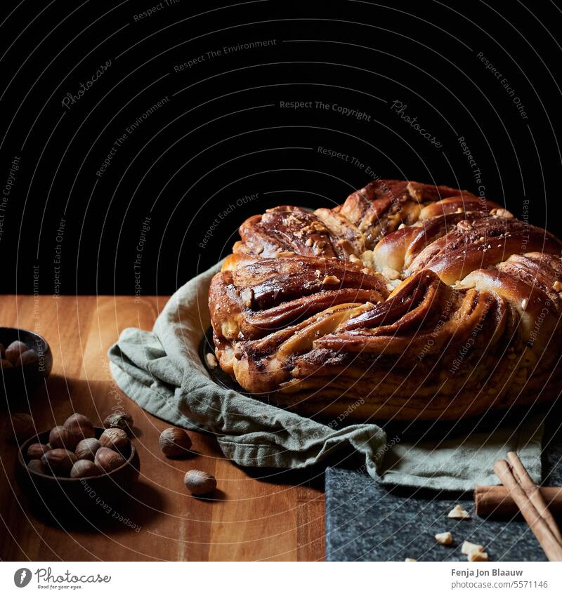 Freshly baked cinnamon bread with a topping of hazelnuts on a wooden kitchen table in a moody setting baker bakery baking cuisine dark and moody food