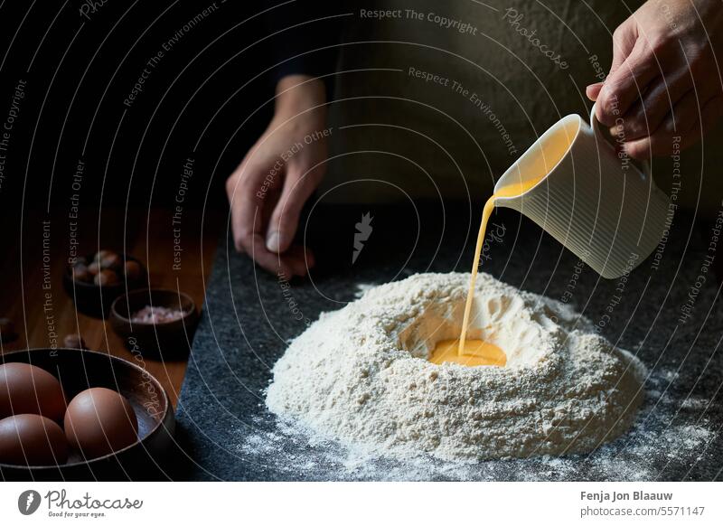 Freshly prepared dough with eggs, handmade kitchen delight in a moody low key light pour shot pouring action making dough process baking studio foek