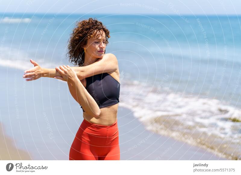 Calm sportswoman stretching arms near sea waves dreamy pensive training workout fitness sportswear warm up beach ocean thoughtful young wellness female exercise