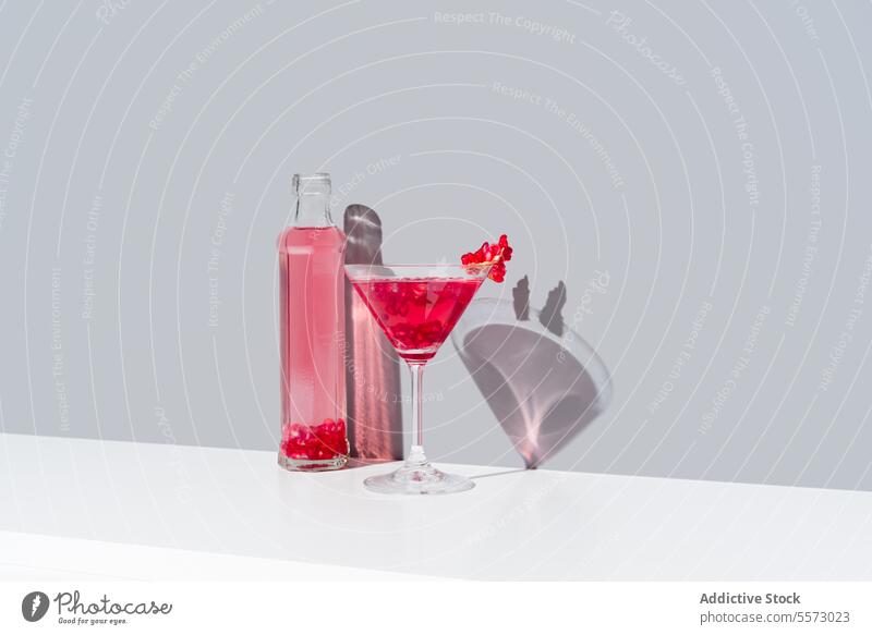 Pomegranate cocktail and bottle duo on gray background glass red garnish backdrop shadow vibrant beverage drink presentation elegant decorative topping