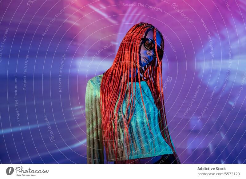 Woman with orange braids standing in neon lights woman young portrait metaverse pose afro braids abstract serious confident appearance sunglasses unemotional