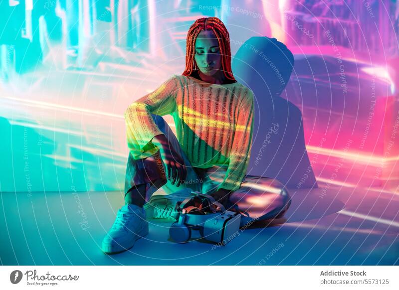 Young woman in modern VR headset vr goggles attractive young orange braids cyberspace virtual futuristic metaverse innovation sitting full body serious