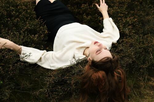 Young woman in white woolen sweater and black skirt lying upside down on a rampart in the heath between grass and heather Woman Large tall woman Slim Bright Joy