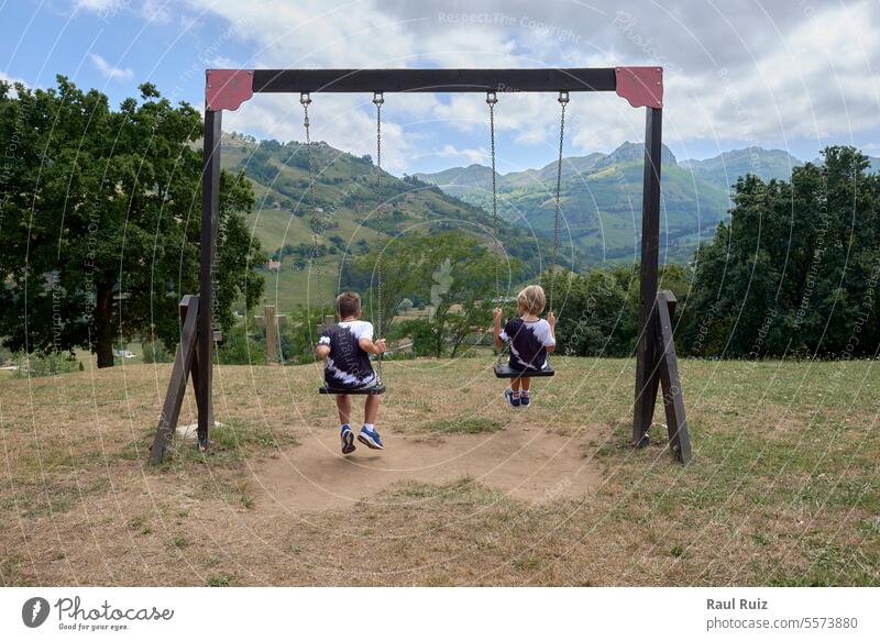 Two children on their backs swinging towards the mountain action enjoyment excitement innocence kindergarten laughing play playful playing preschool recreation
